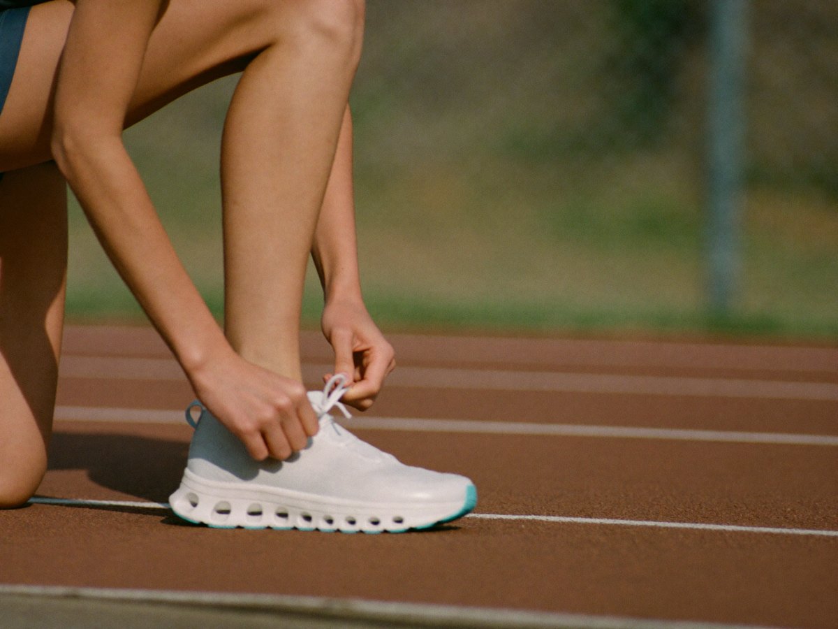 Athlete kneeling on a track, tying a running shoe